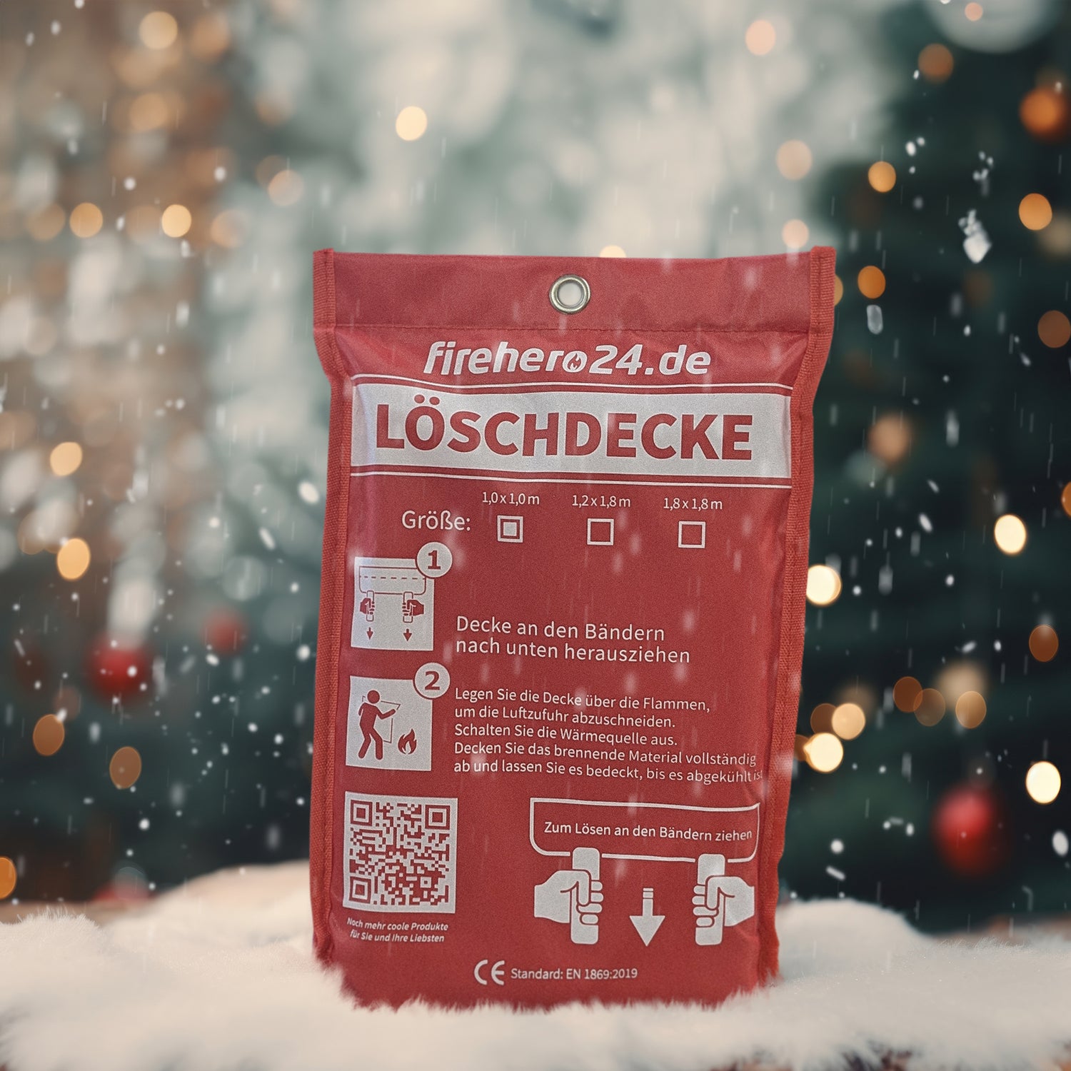 Feuerlöschdecke als Weihnachtsgeschenk vor festlichem Hintergrund mit Schneefall und Tannenbaum